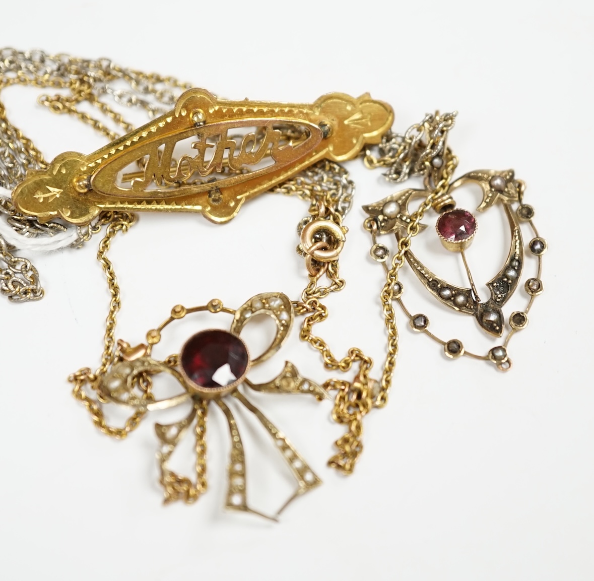 An early 20th century 9ct, garnet and seed pearl set pendant necklace, 43cm, one other similar 9ct and gem set pendant, on a gilt metal chain and a yellow 'metal 'mother' brooch. Condition - fair